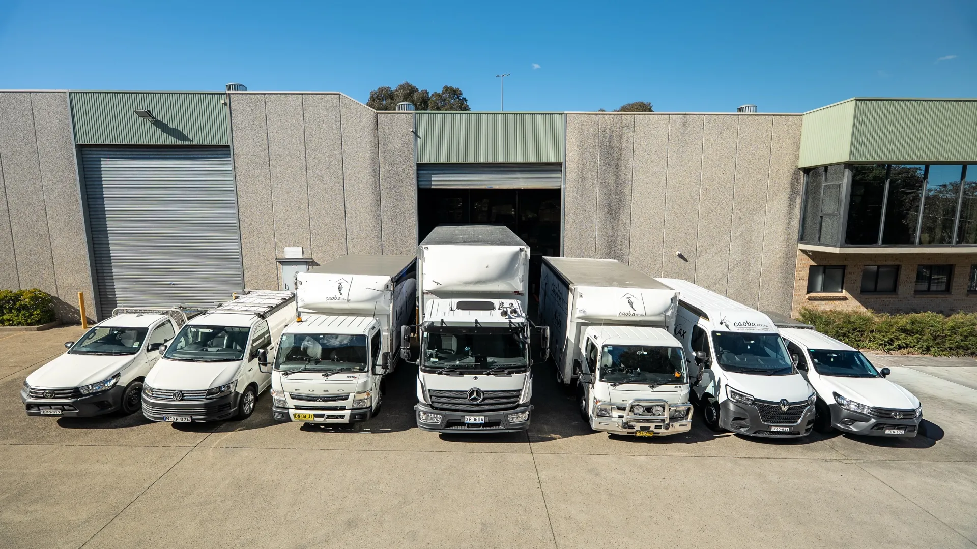Trucks, vans and utes from the fleet parked in front of the open warehouse door